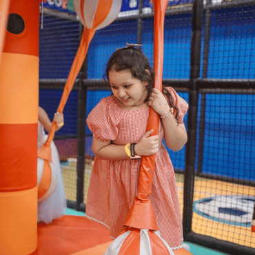Girl enjoying a rope swing activity at an indoor kids play area.